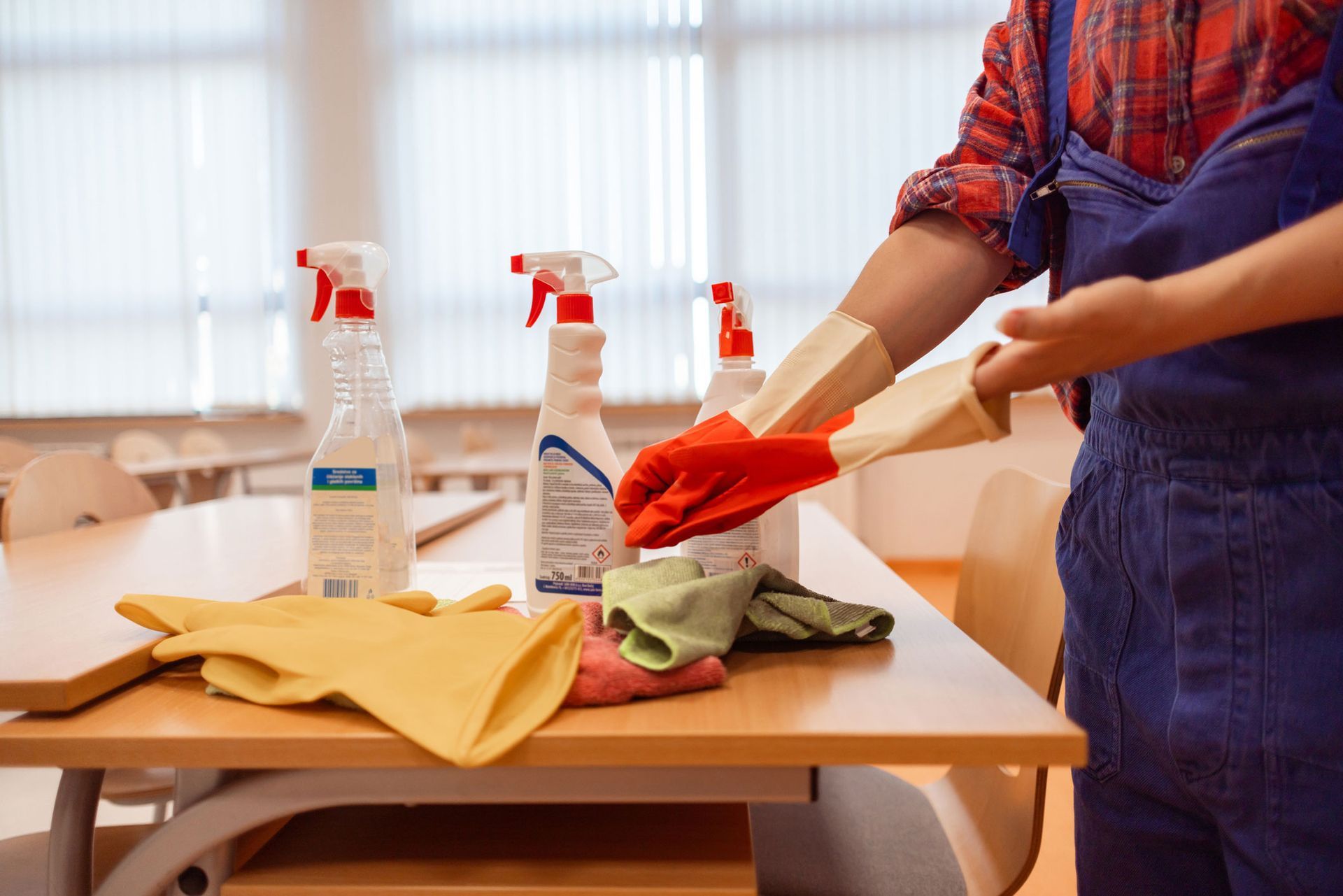 A person is cleaning a desk in a classroom with cleaning supplies.