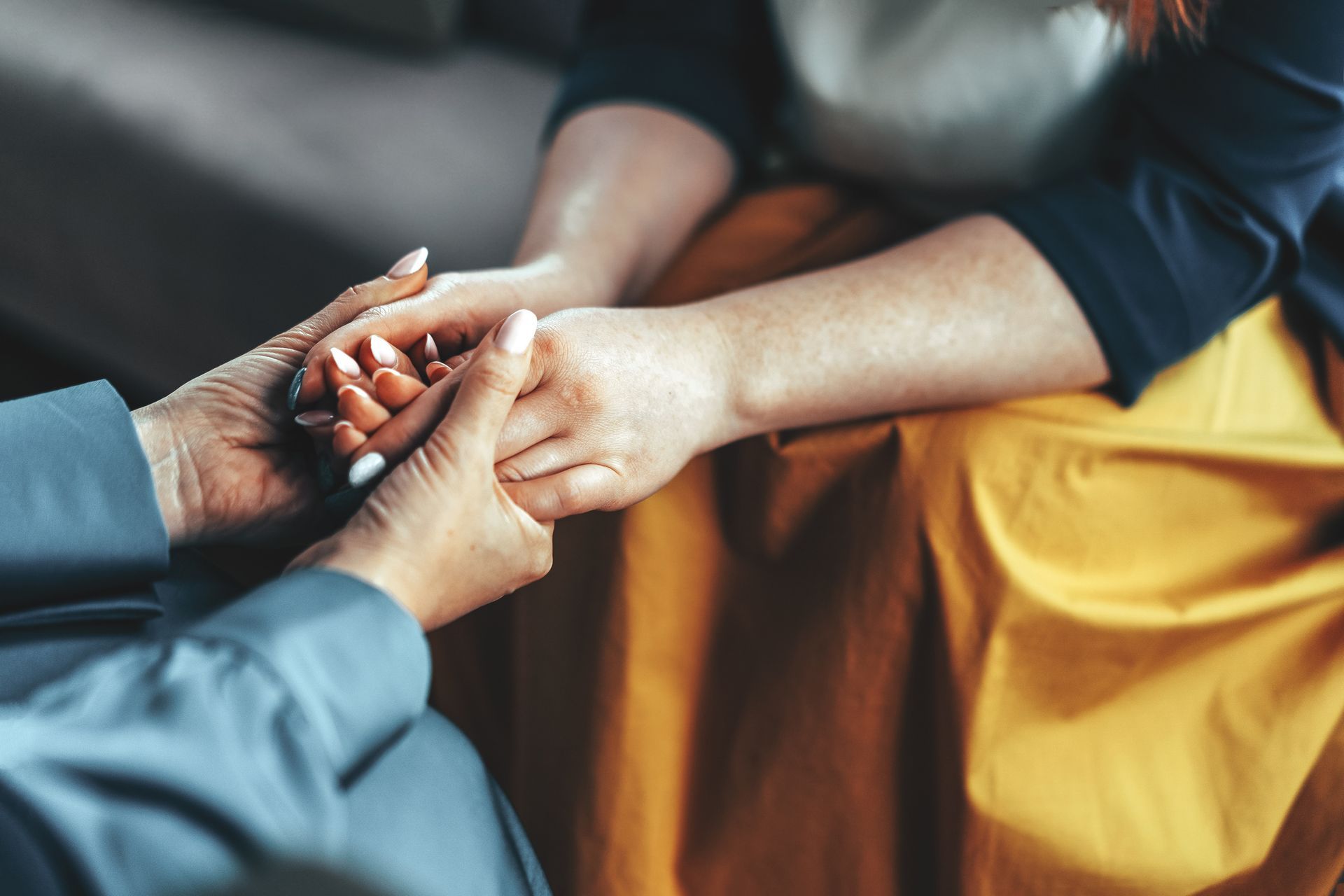 A woman is holding another woman 's hand while sitting on a couch.