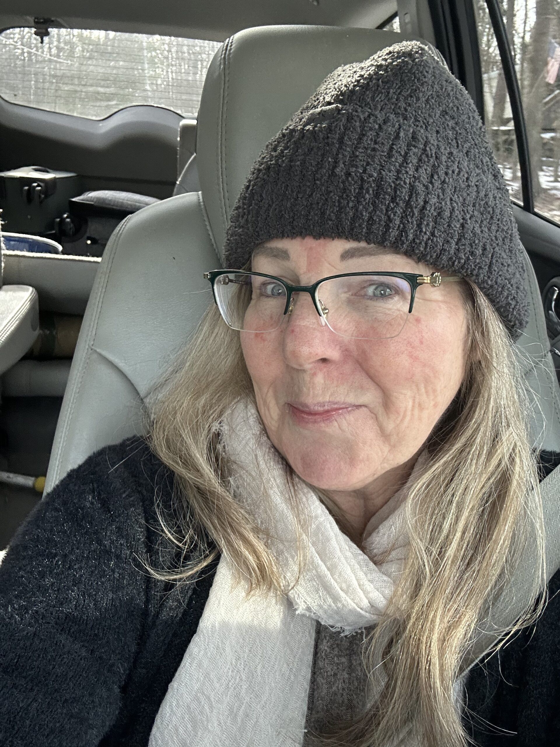A woman wearing a hat and scarf is sitting in the back seat of a car.