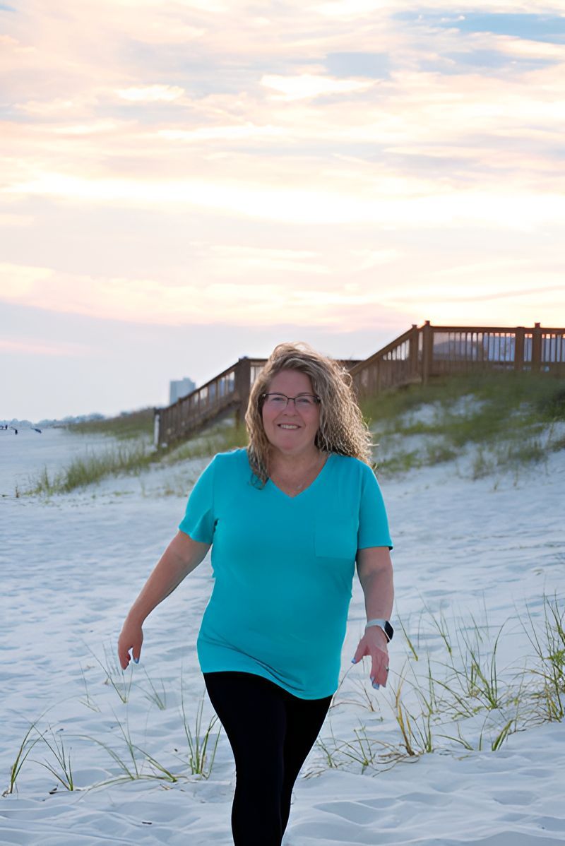 A woman in a blue shirt is walking on a sandy beach.
