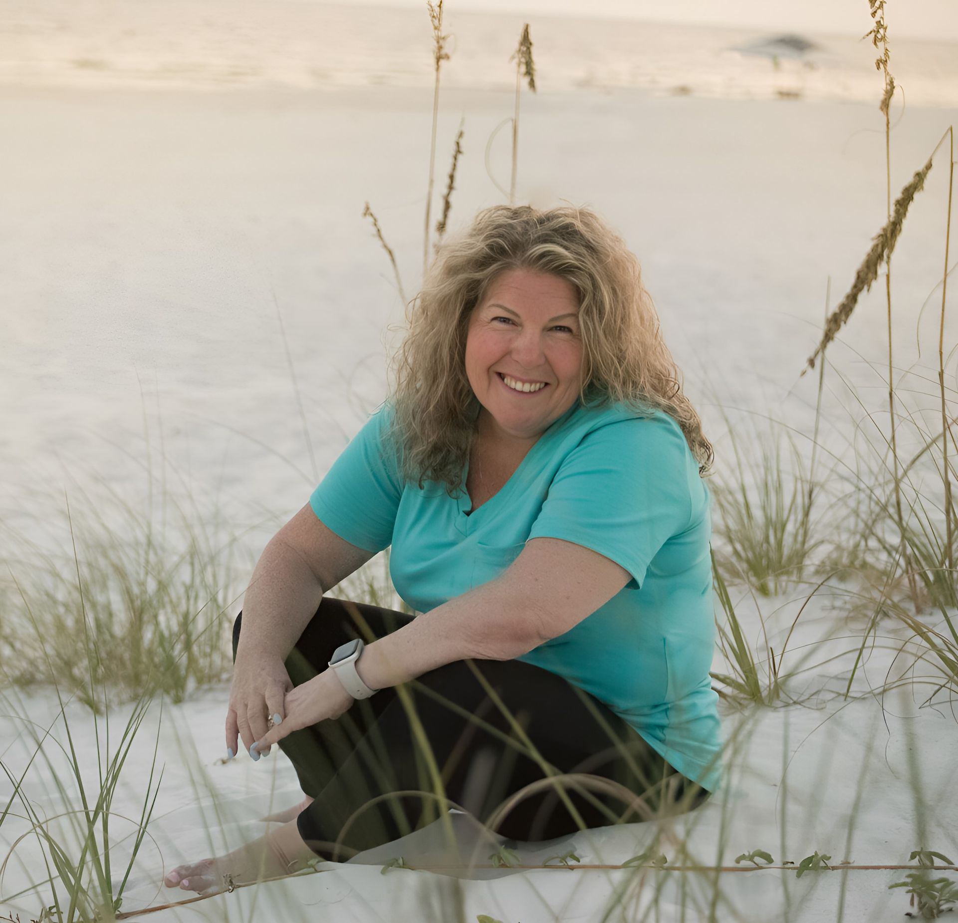 A woman in a blue shirt is sitting on the beach