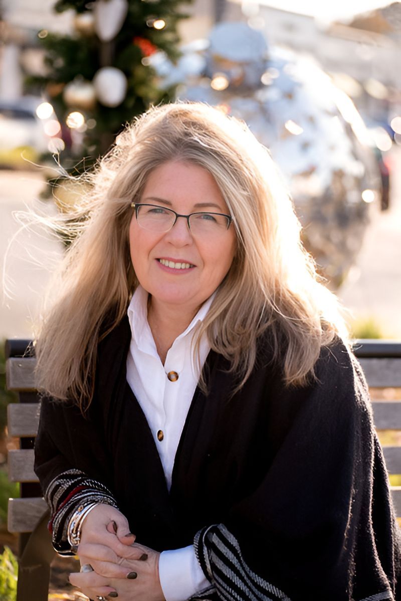 A woman wearing glasses is sitting on a bench in front of a christmas tree.