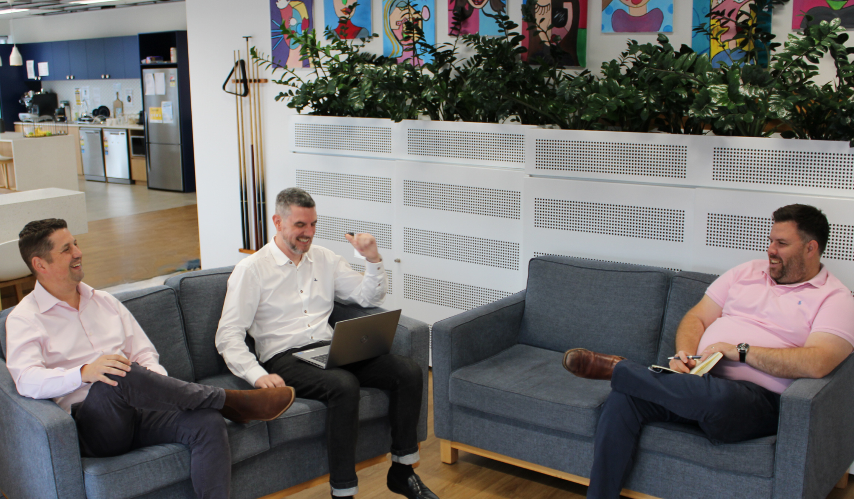 Three men are sitting on a couch talking to each other.