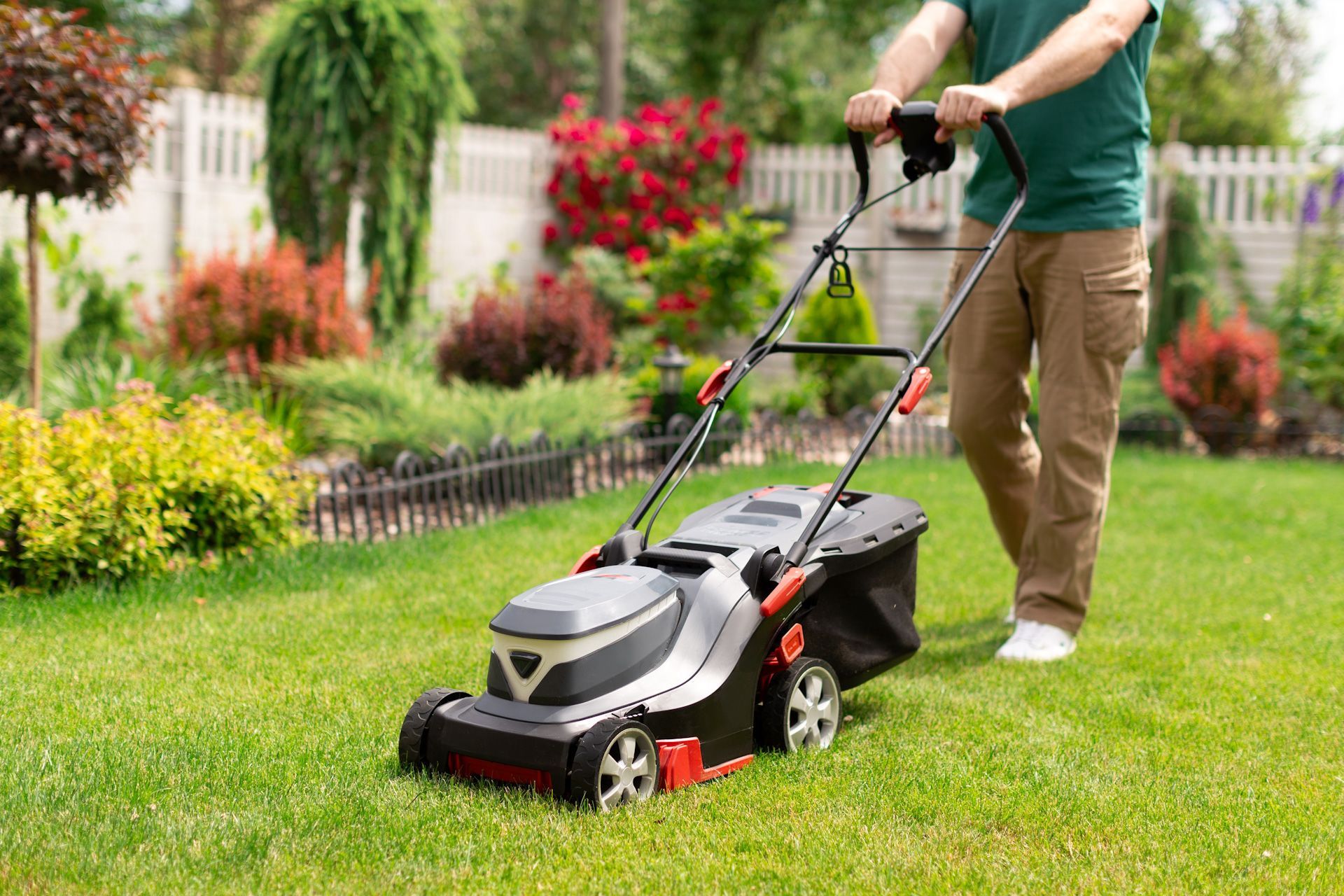 A man is mowing his lawn with an electric lawn mower.