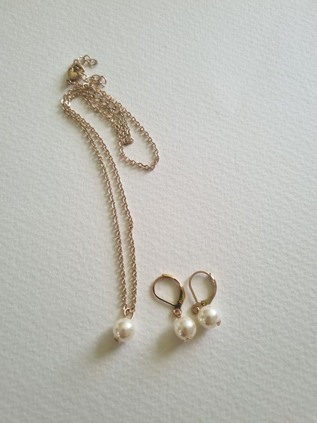 Collar de oro con colgante de cruz y pendiente a juego sobre superficie blanca.