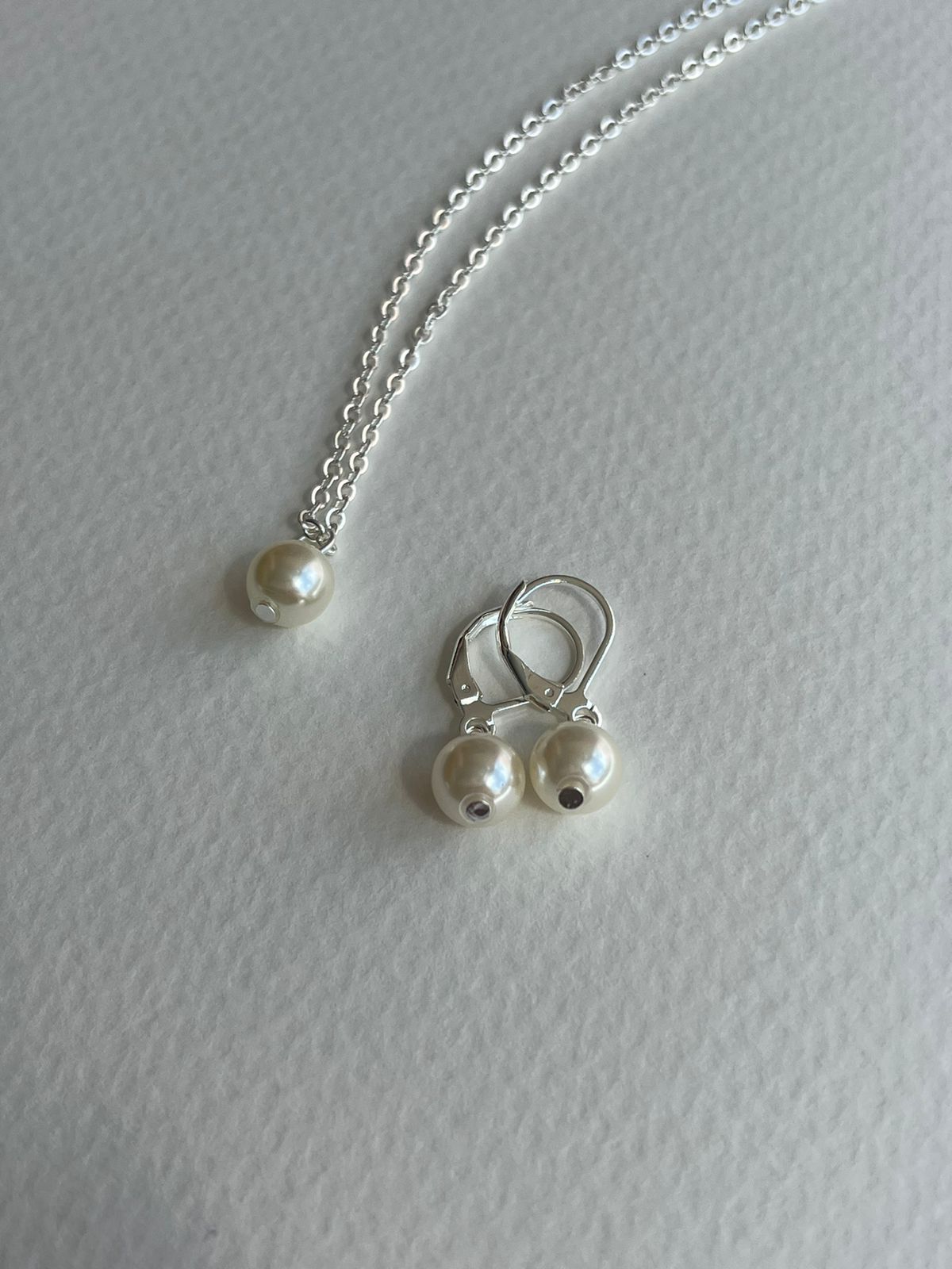 Pendientes dorados en forma de corazón exhibidos sobre una tarjeta blanca con un logotipo, colocada sobre una superficie de madera.