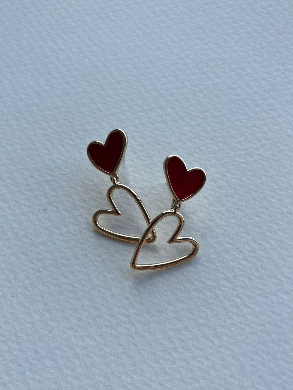 Pendientes de corazón rojo sobre tarjeta blanca con detalles dorados, diseño floral y texto en español.