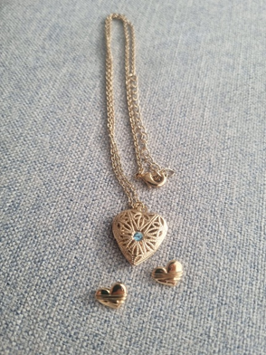 Collar con colgante de corazón dorado y pendientes de corazón a juego sobre tela azul.