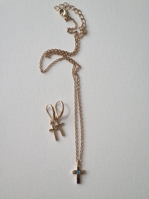 Collar de oro con colgante de cruz y pendiente a juego sobre superficie blanca.