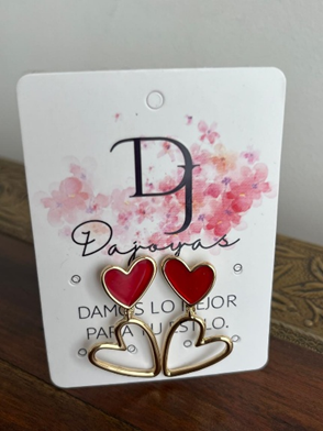Pendientes de corazón rojo sobre tarjeta blanca con detalles dorados, diseño floral y texto en español.