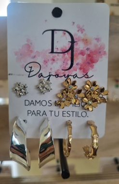 Juego de pendientes con cinco pares: de botón, florales, de aros dorados y pendientes curvos de plata, sobre cartulina blanca.
