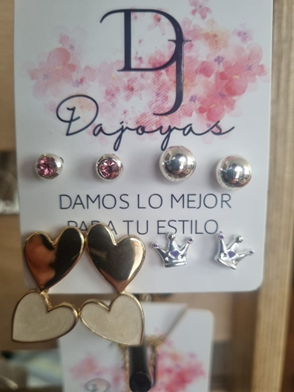 Juego de pendientes: varios pendientes con corazones y coronas, sobre cartulina rosa y blanca.