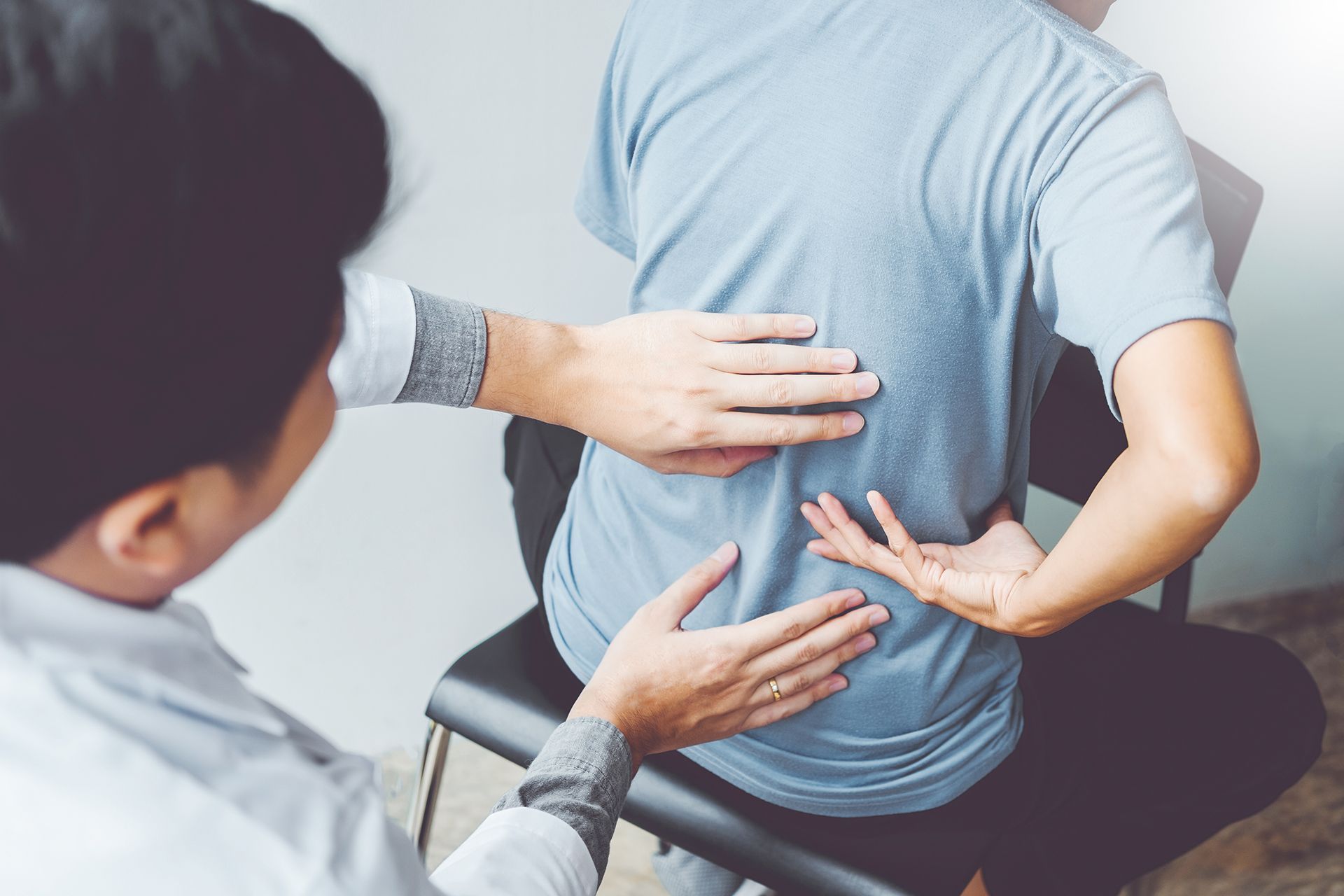 A man is sitting in a chair while a doctor examines his back.