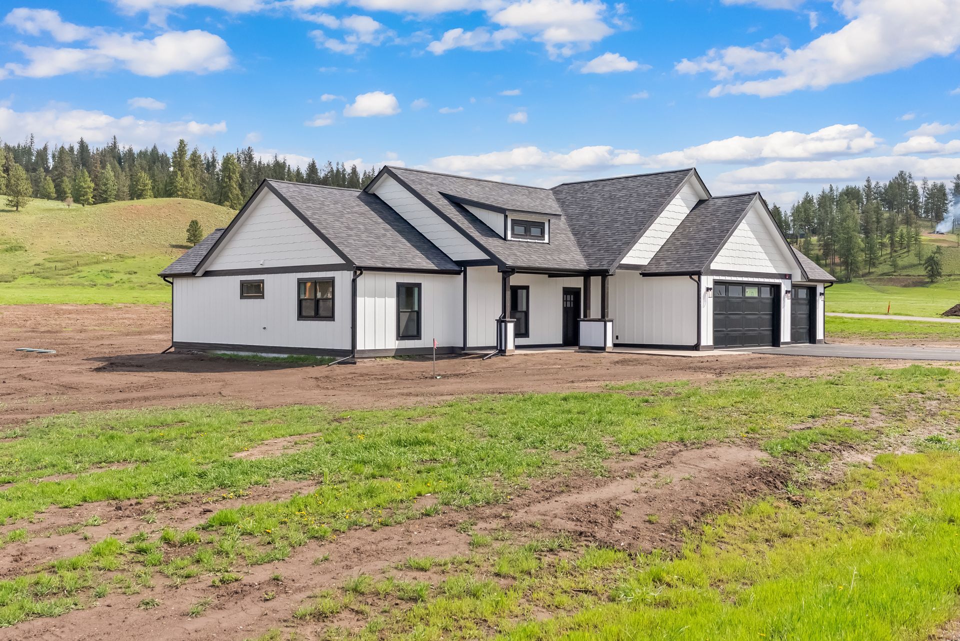 New white house with dark roof in a grassy, open field under a blue sky