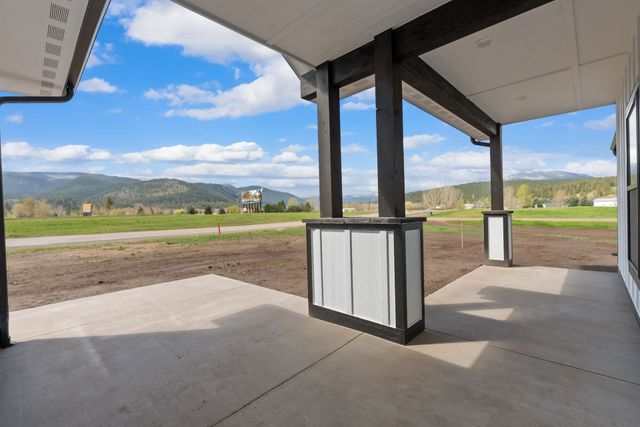 Covered concrete patio with black support posts overlooking fields and mountains under a blue sky