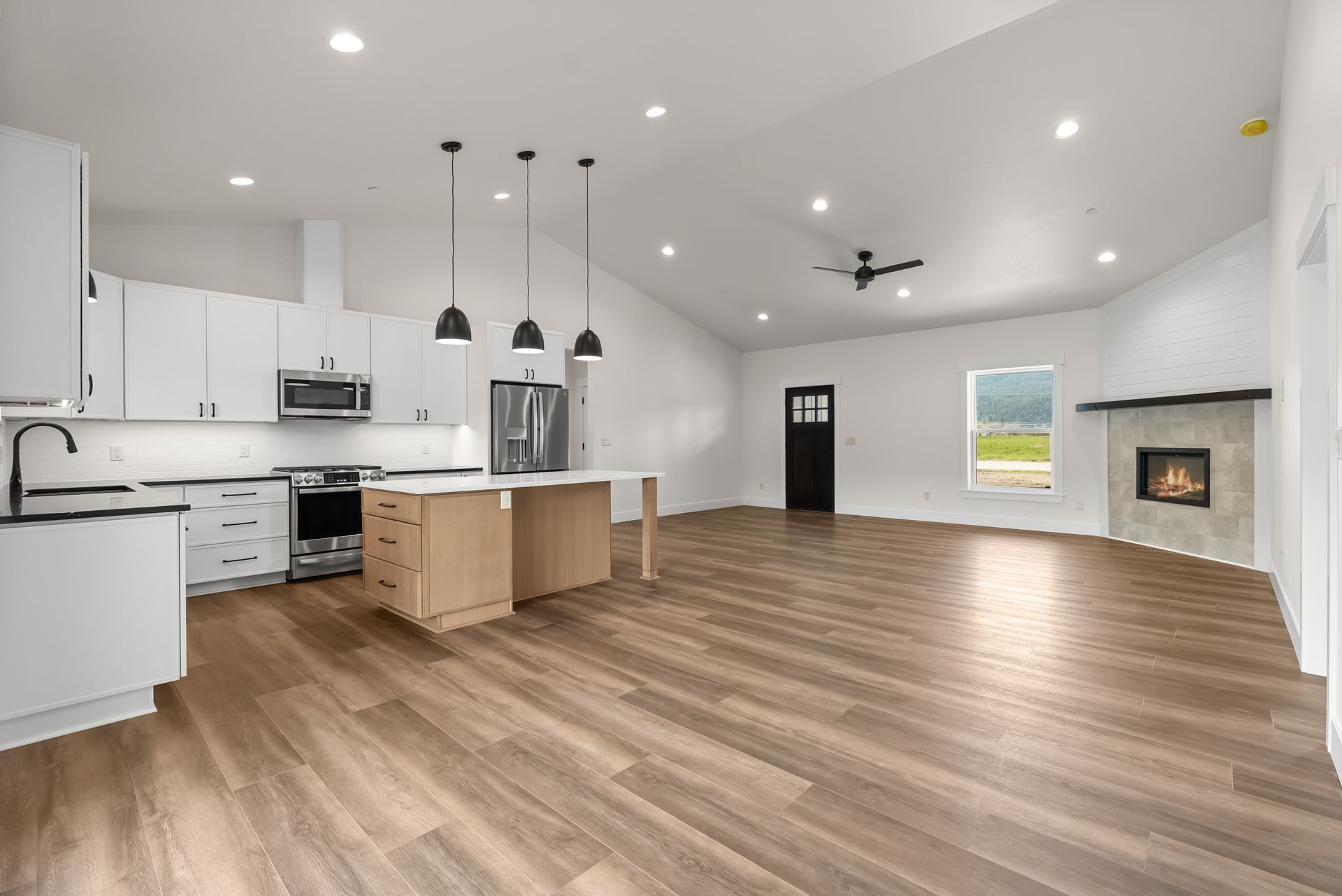 Open-plan kitchen and living room with white cabinets, wood floors, island, ceiling lights, and a fireplace.