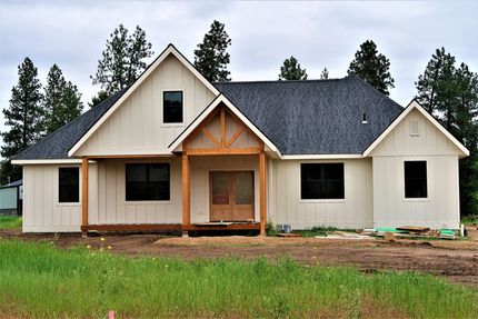 New beige house under construction with dark roof and front porch on a grassy lot
