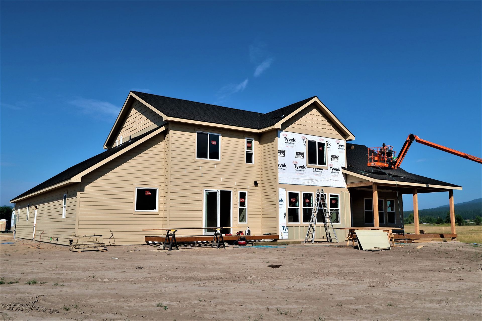 Two-story beige house under construction with scaffolding and a crane against a clear blue sky