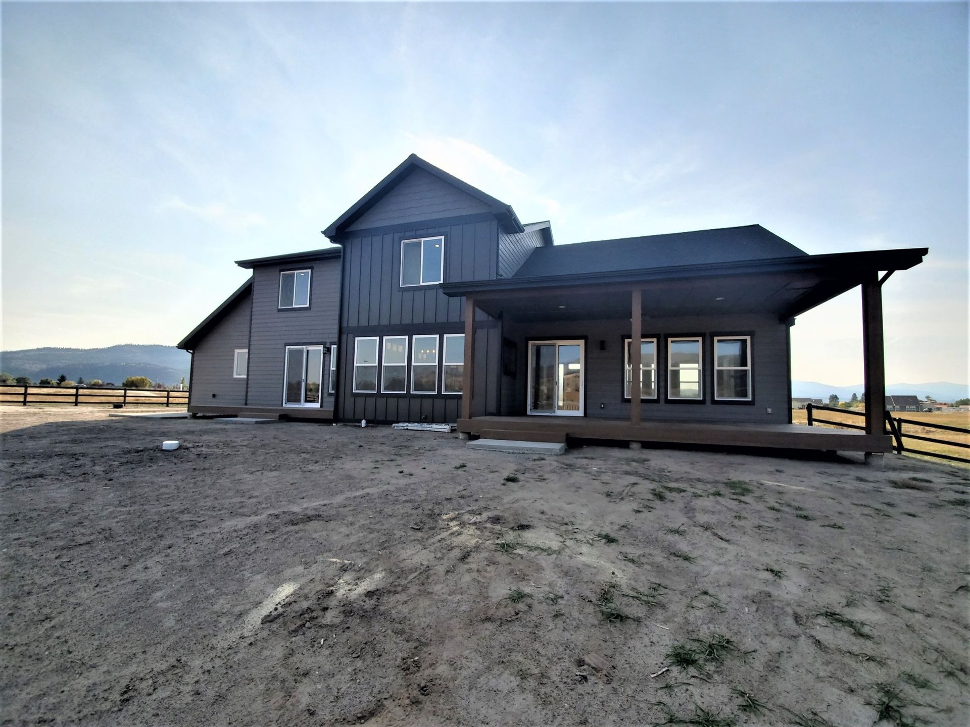 Modern dark-gray house with a covered porch on a sandy lot under a bright sky