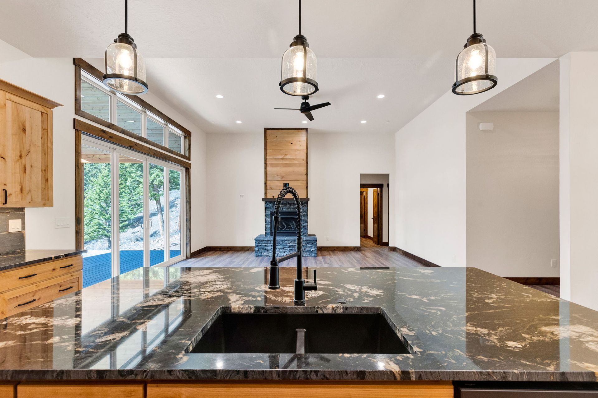 Modern kitchen with black granite island, pendant lights, large windows, and an open living area