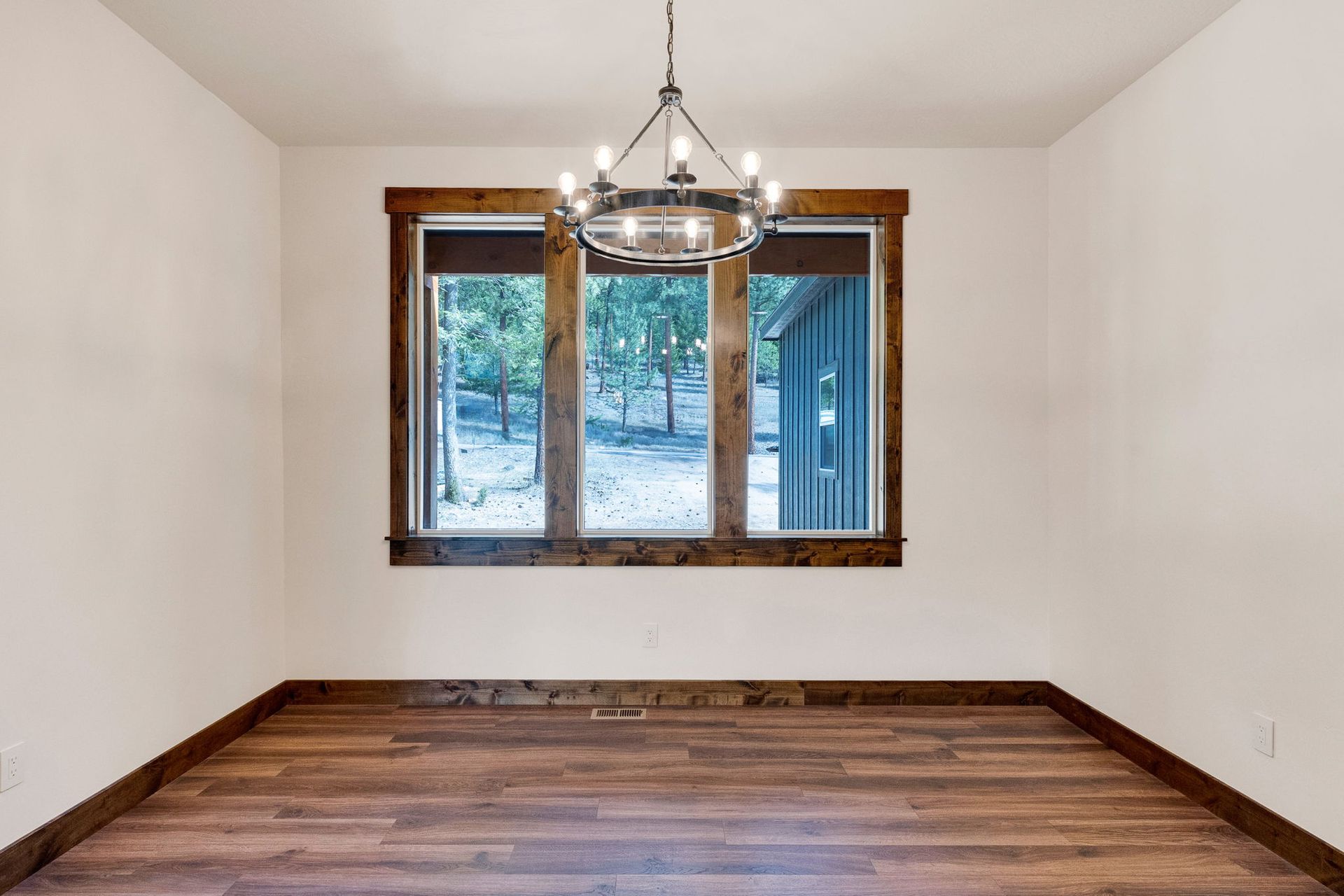 Empty room with hardwood floor, white walls, and a window with a chandelier overhead.
