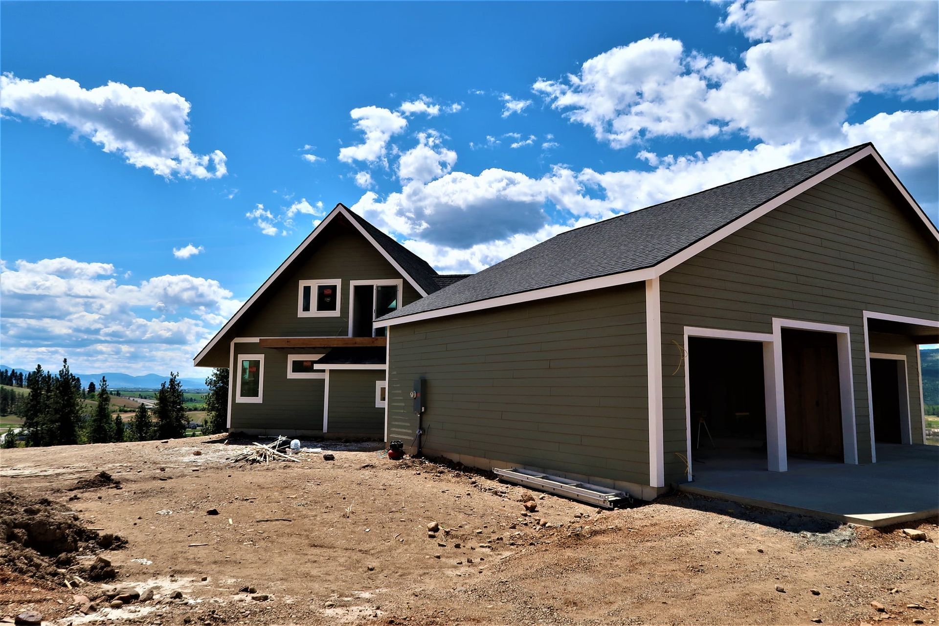 New house and detached garage under a blue sky with clouds in a dirt lot