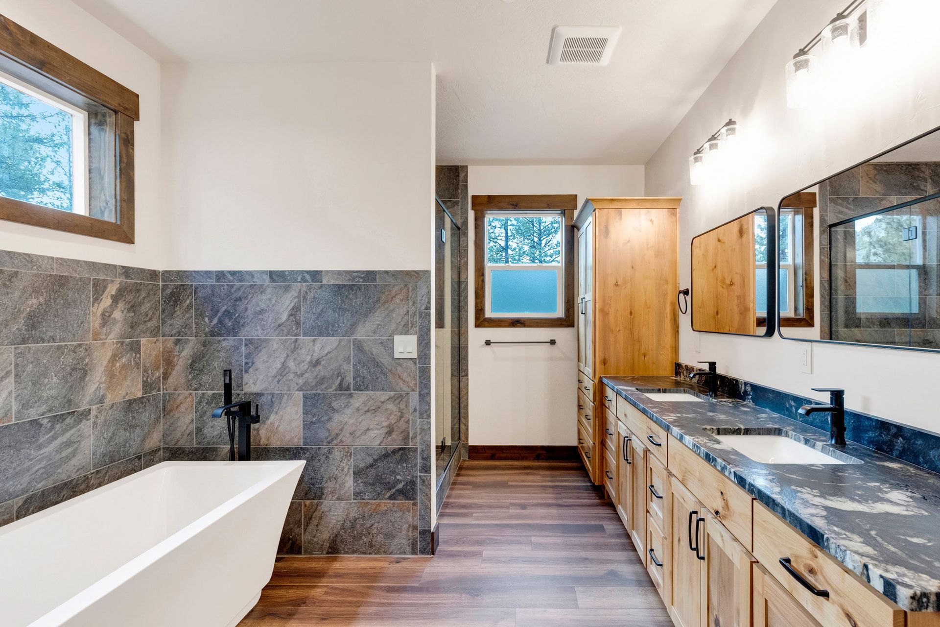 Modern bathroom with freestanding tub, marble-tiled shower, wood vanity, and large mirror.