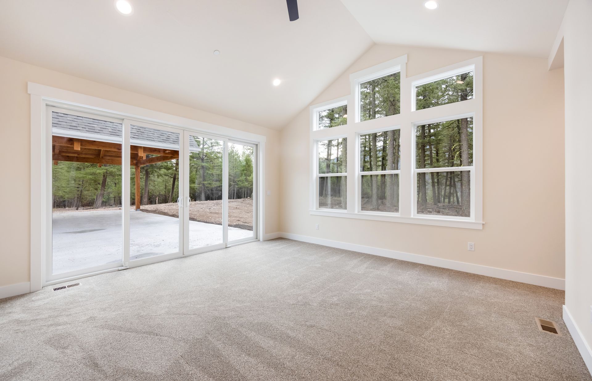 Empty carpeted living room with large windows and sliding glass doors to a patio