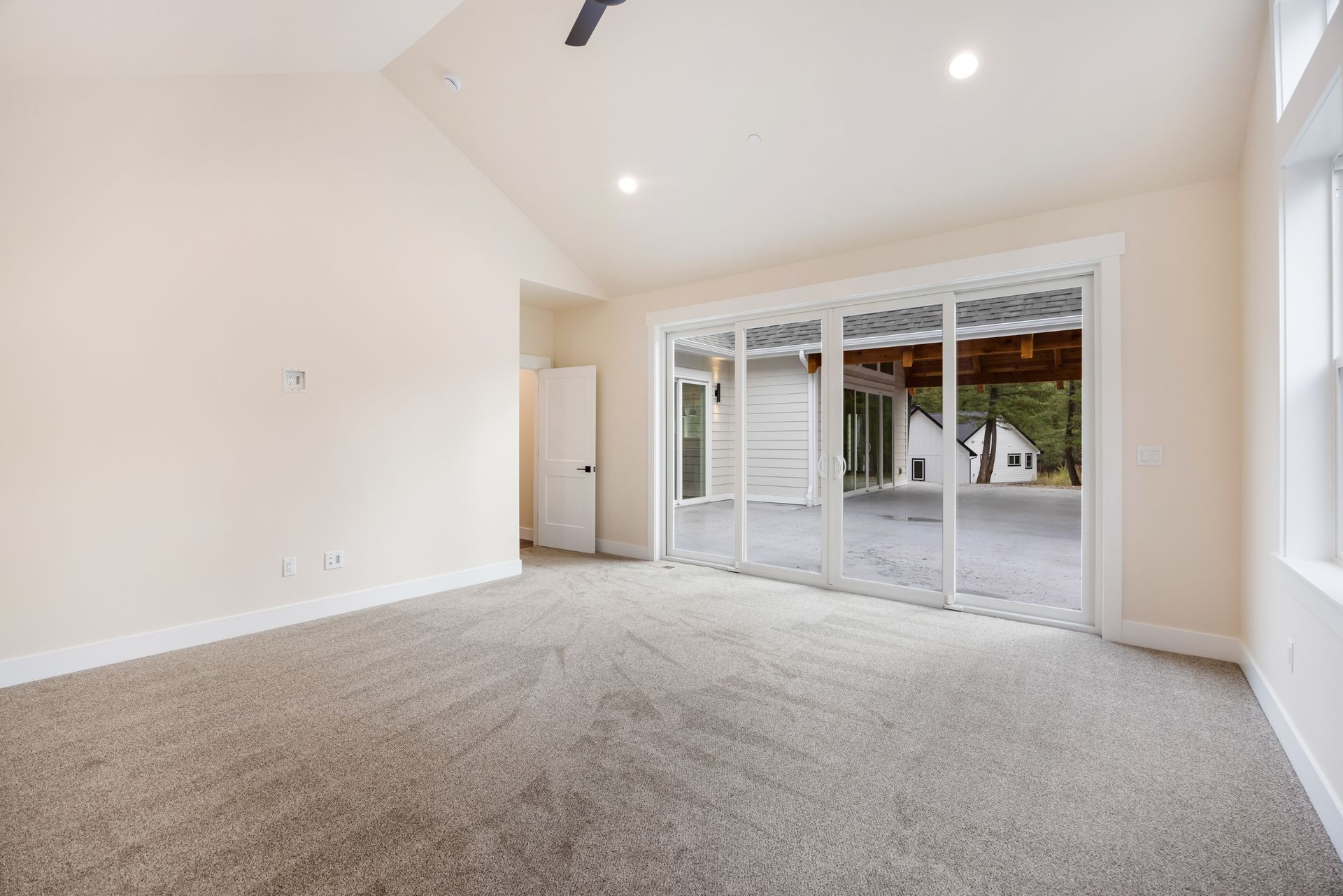 Empty beige living room with carpet, recessed lighting, and sliding glass doors to a patio.