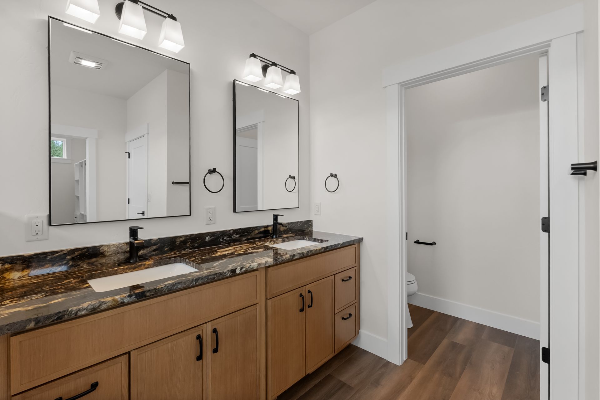 Modern bathroom vanity with double mirrors, granite countertop, and white door on wood flooring