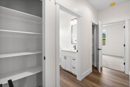 Bright hallway with open closet shelves and a bathroom vanity, leading to a sunlit bedroom.