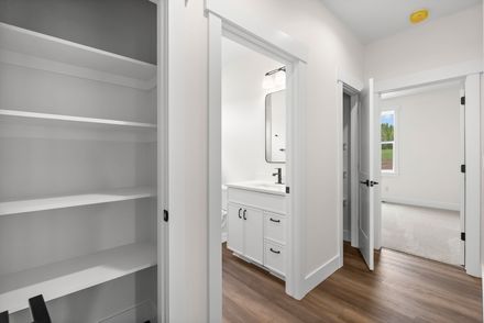 Bright hallway with open closet shelves and a bathroom vanity, leading to a sunlit bedroom.