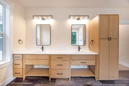 Modern bathroom vanity with double sinks, mirrors, wall lights, and a tall wooden storage cabinet