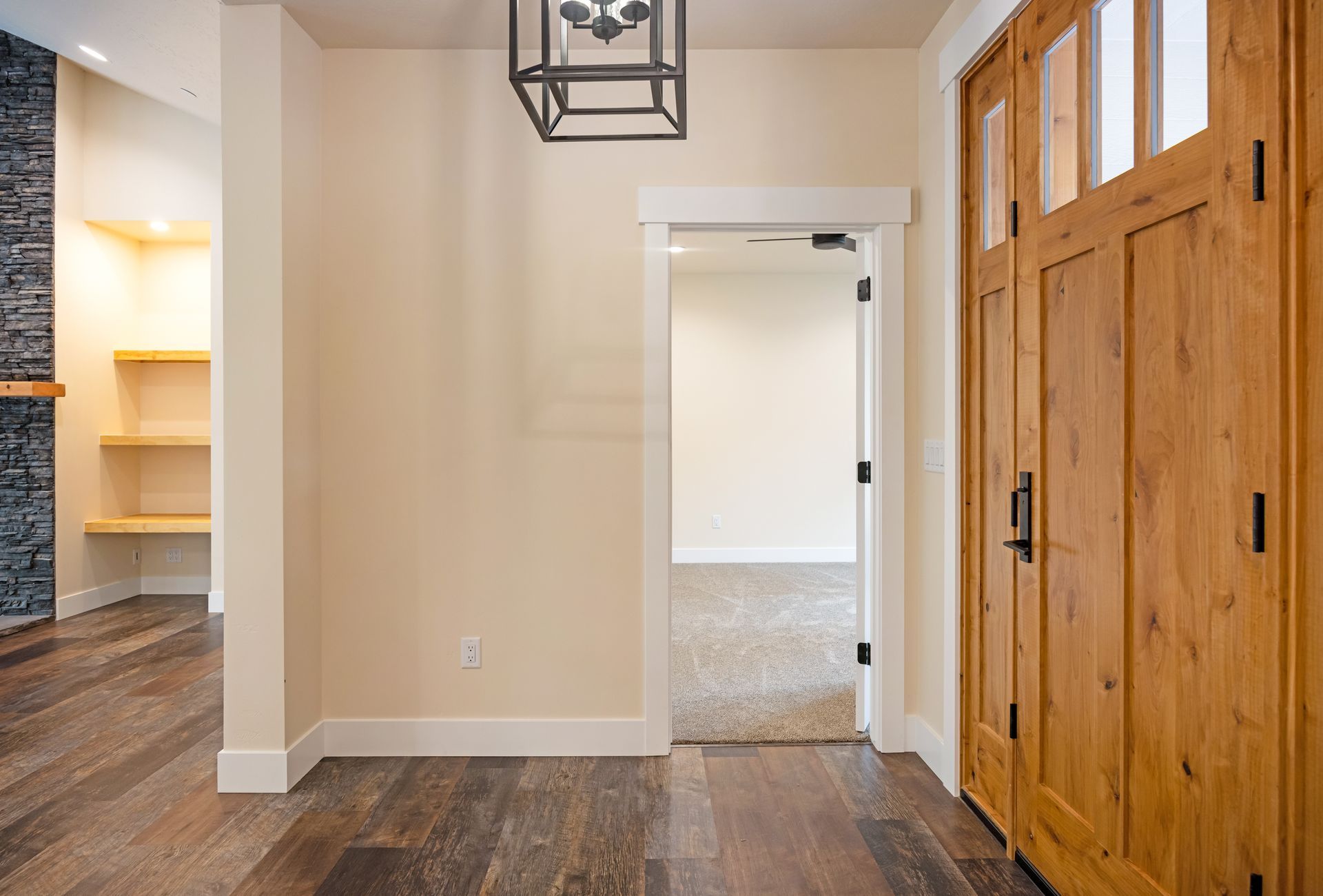 Entryway with wood doors, beige walls, dark hardwood floors, and a view into a bright room.