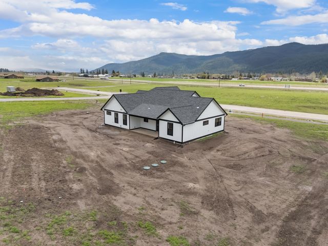 Small white house with black roof on a bare lot, with mountains and open fields in the background.