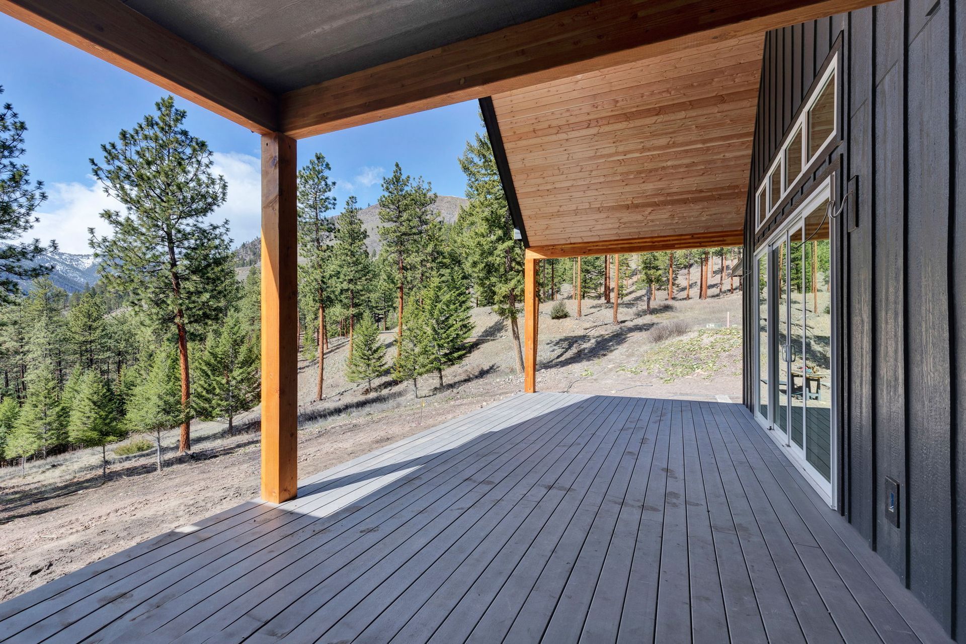 Covered wooden deck overlooking pine trees and a rocky hillside under a bright blue sky