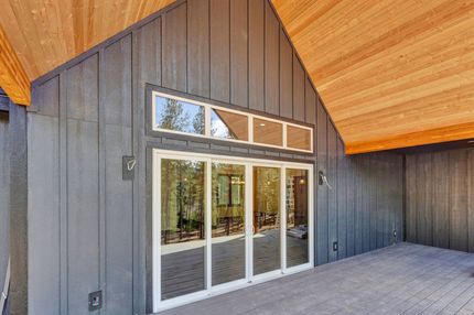 Modern outdoor patio with sliding glass doors, dark wood siding, and a wood-paneled overhang