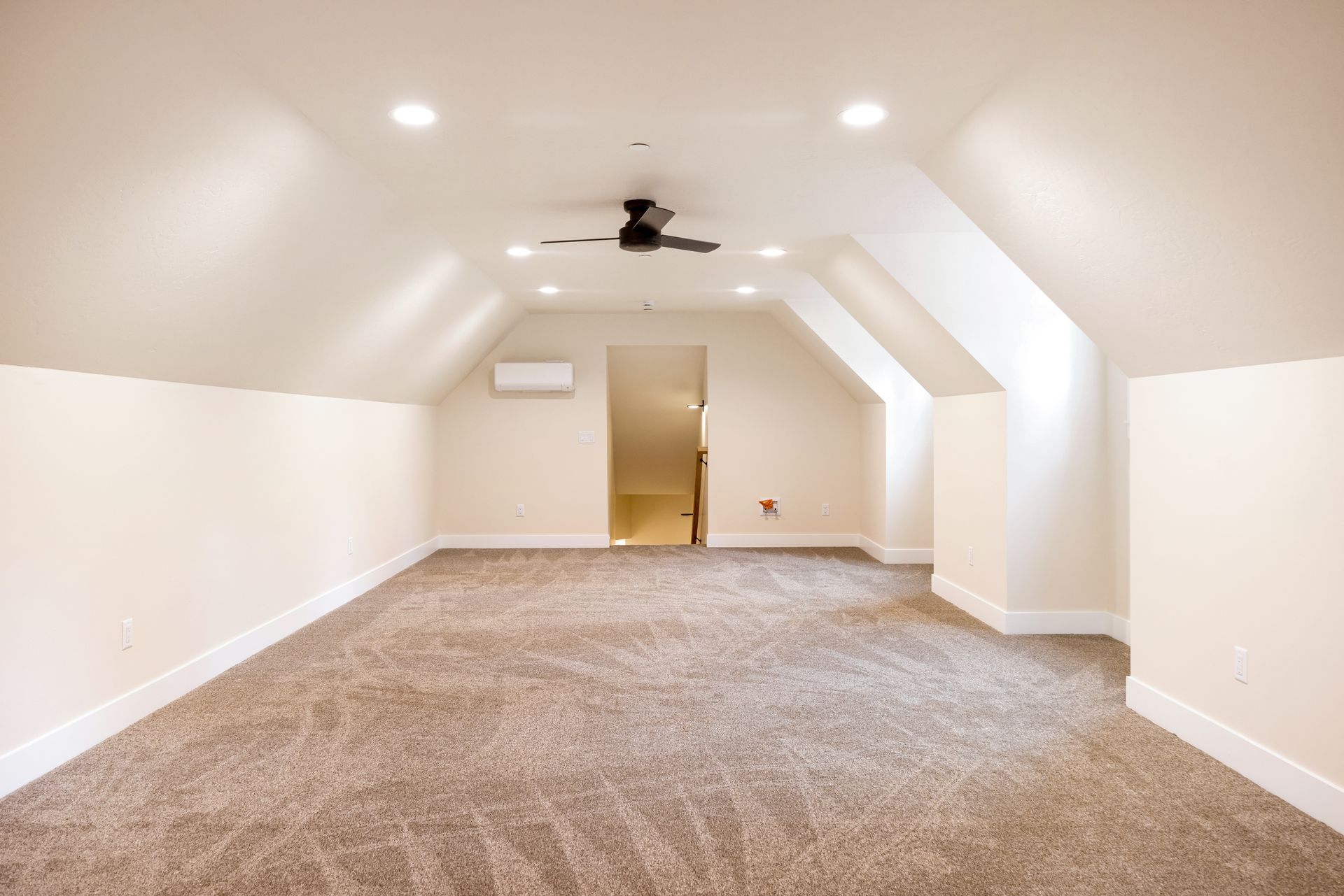 Empty carpeted attic room with sloped white ceiling, recessed lights, ceiling fan, and wall AC unit