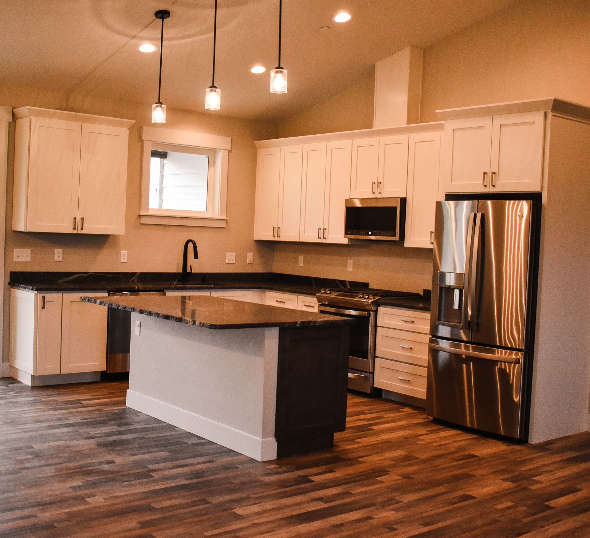 Modern kitchen with white cabinets, stainless steel appliances, and a central island with dark countertops.