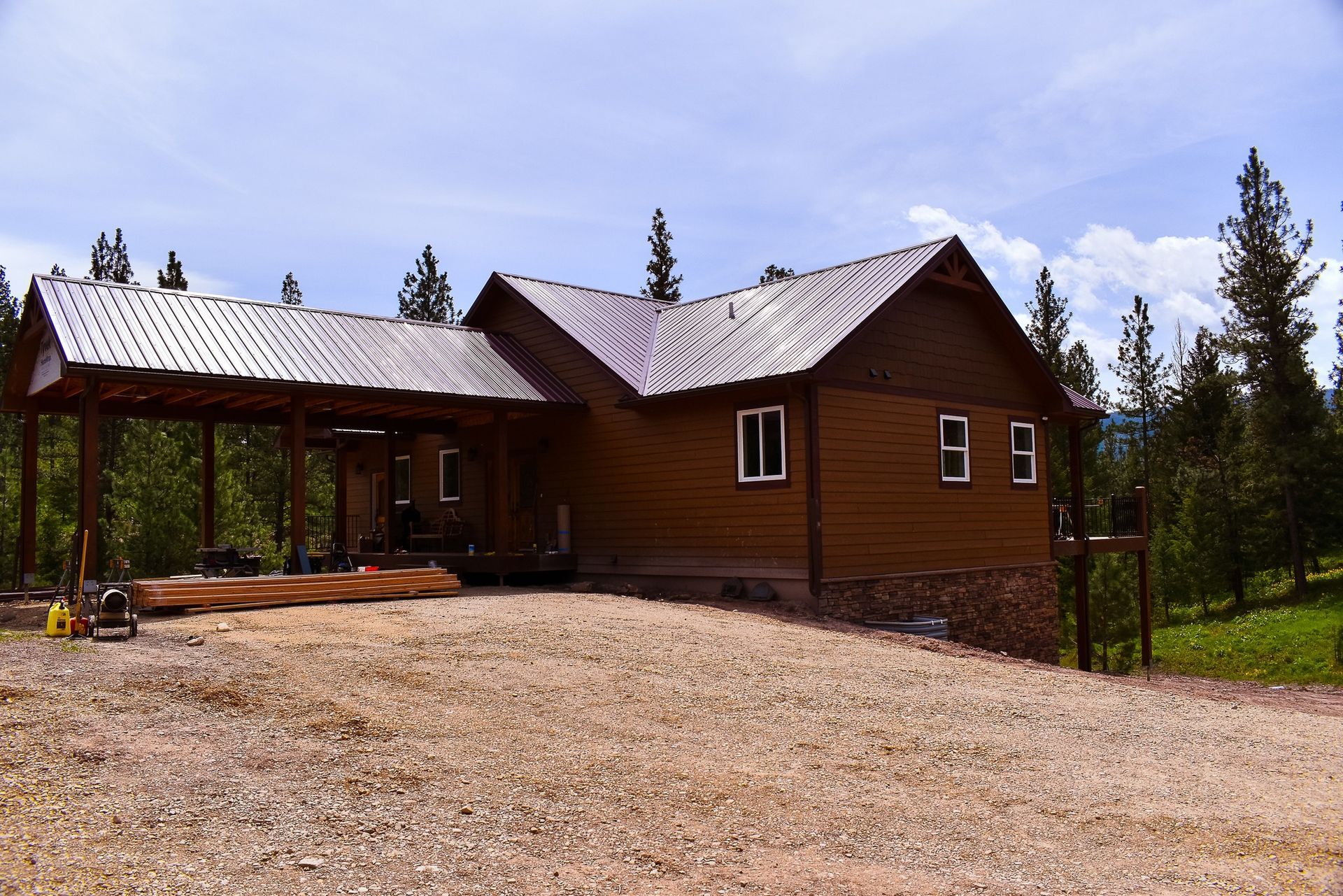 Rustic wooden cabin with a metal roof beside a gravel driveway under a cloudy sky