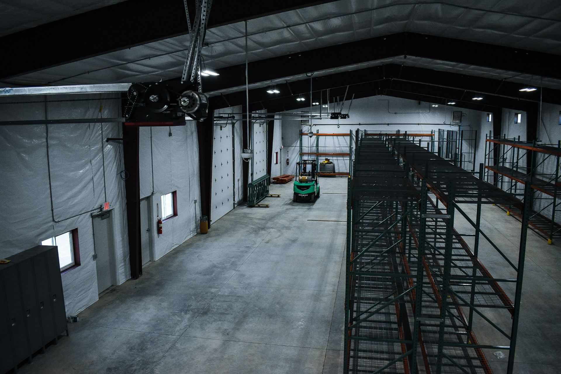 Empty industrial warehouse with a green forklift and metal shelving on the right