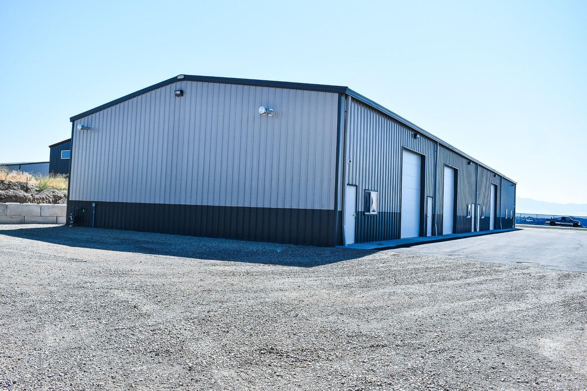 Large gray industrial warehouse on a gravel lot under a clear blue sky