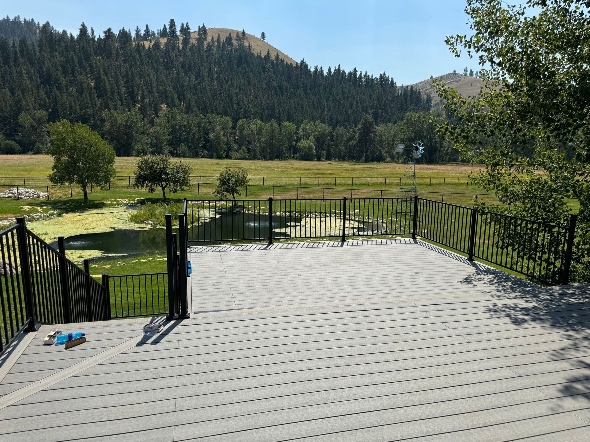 Wooden deck overlooking a fenced grassy field and forested hills under a clear blue sky