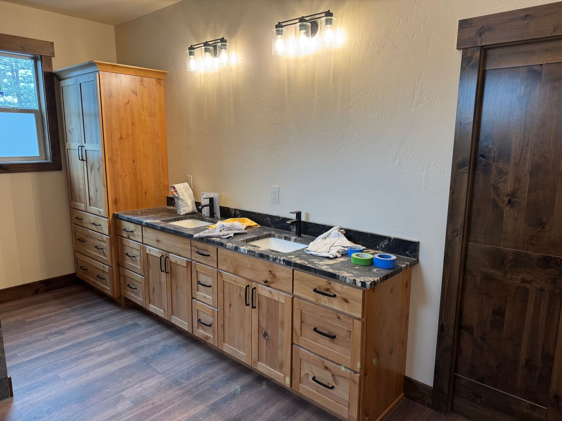 Modern bathroom with double vanity, wood cabinets, black countertop, mirrors, and wall sconces