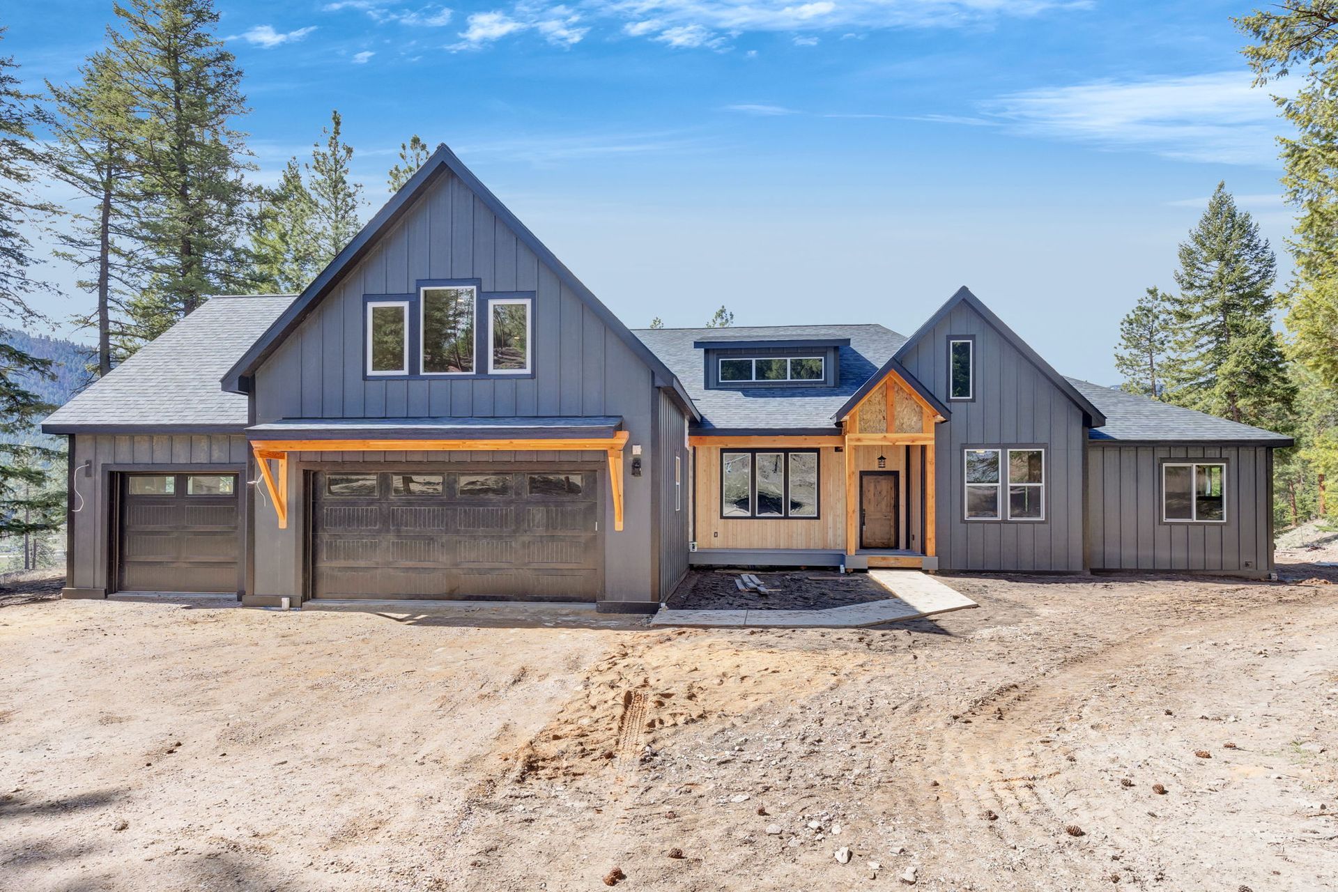 Modern gray house with wood accents, large garage doors, and a front porch in a wooded setting