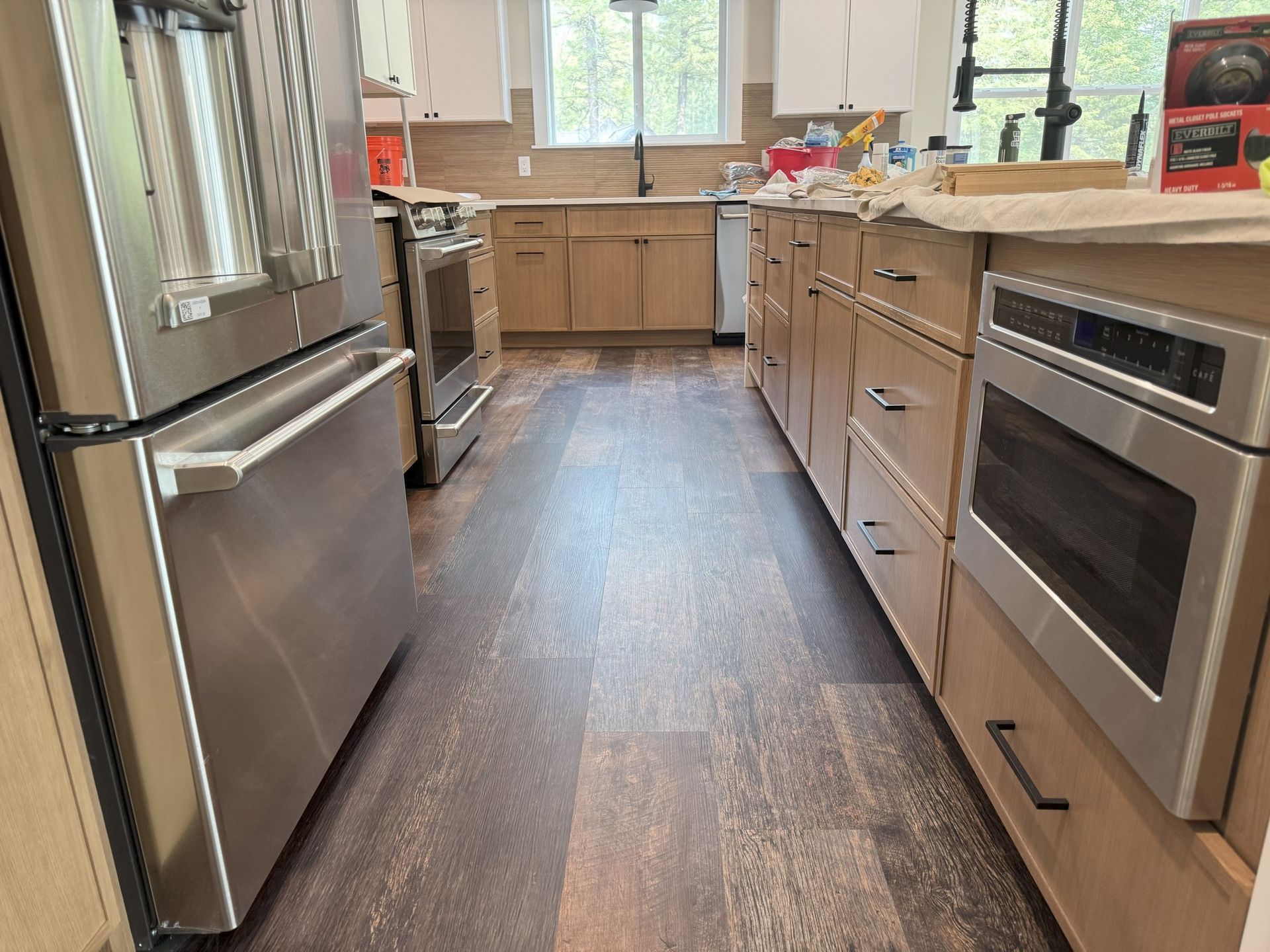 Modern kitchen with stainless appliances, wood cabinets, and a long dark floor leading to a bright window.