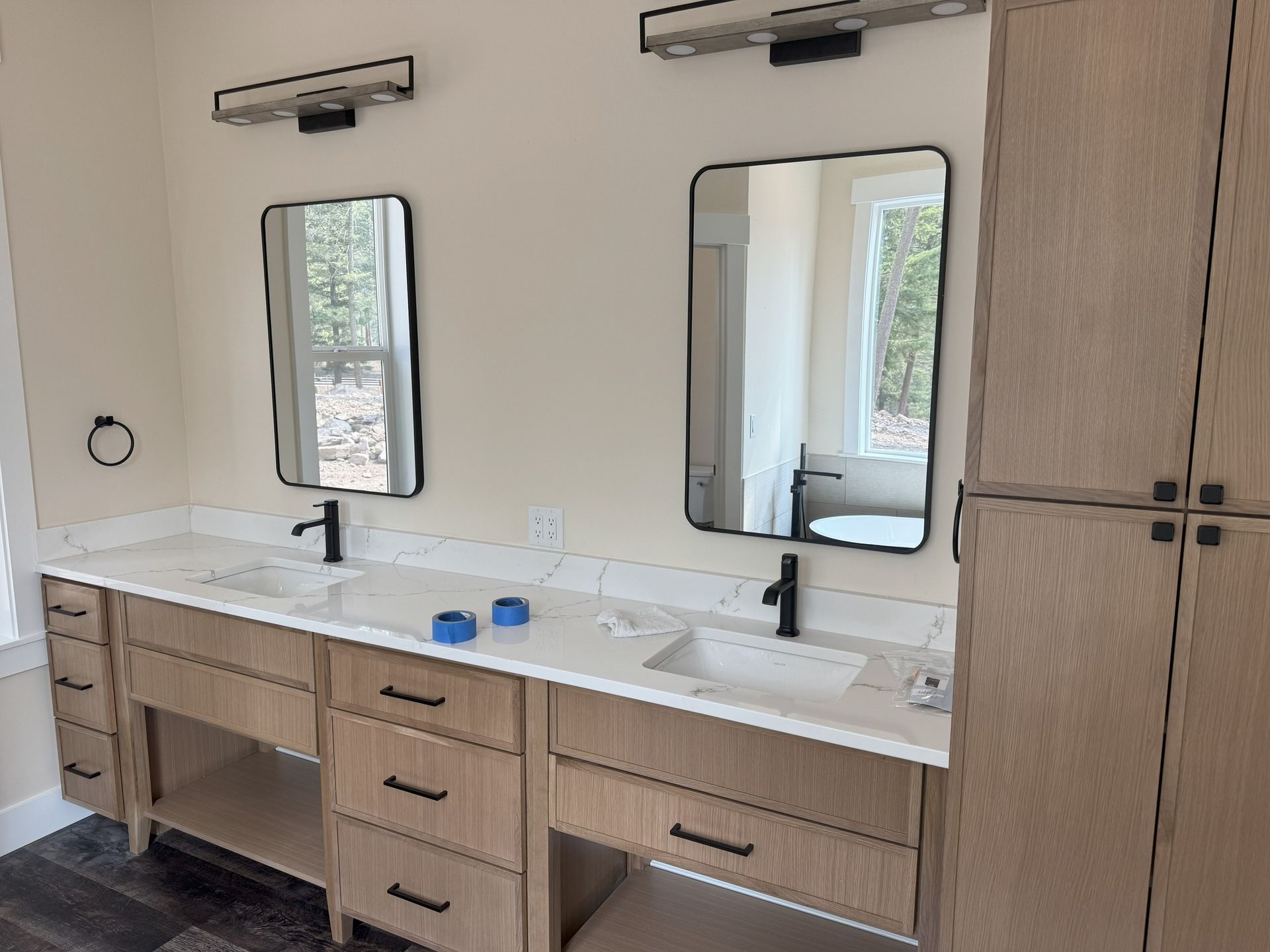 Modern double vanity with wood cabinets, white countertops, black faucets, and mirrors in a bright bathroom