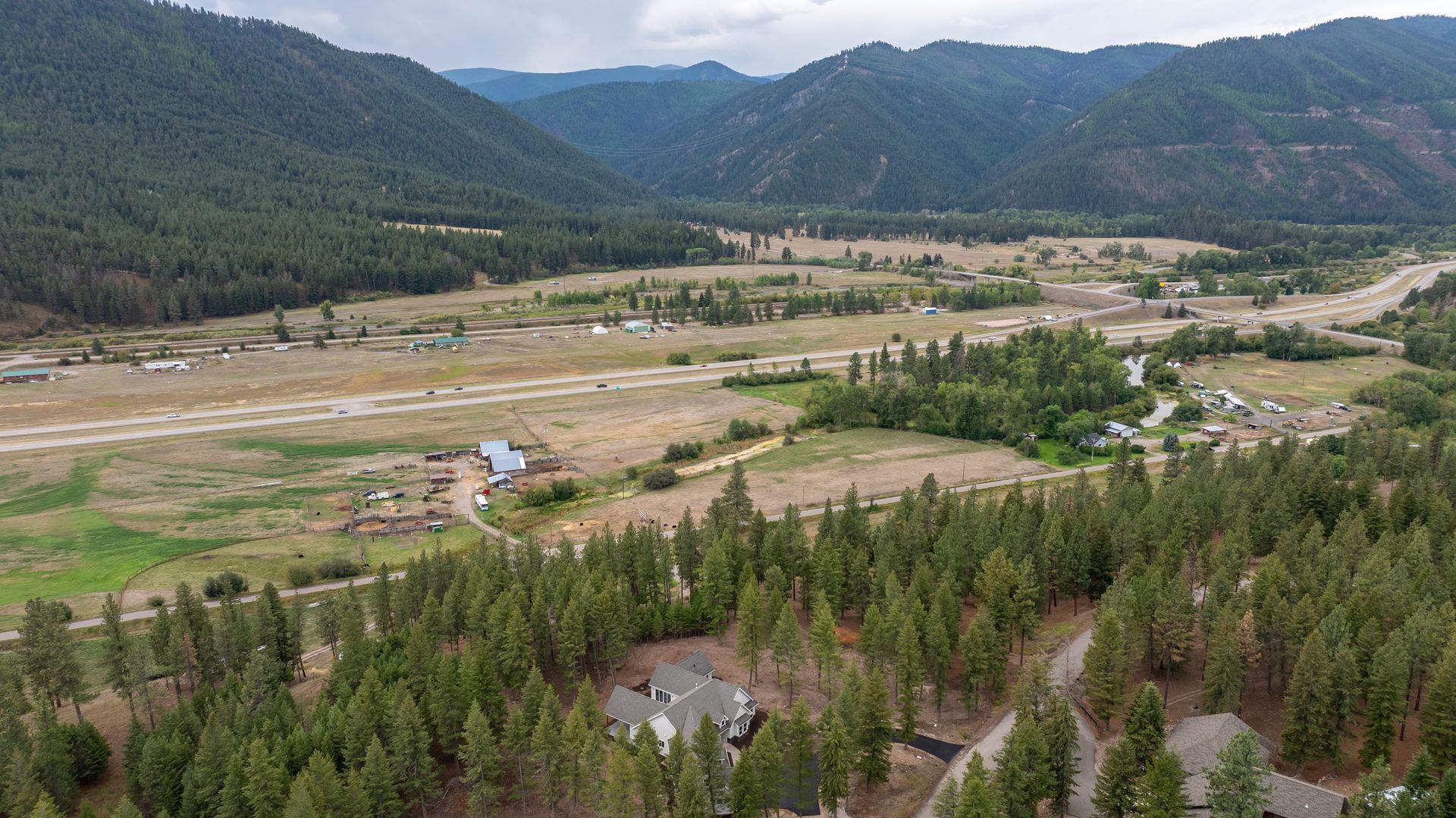 Mountain valley with a wide meadow, scattered buildings, and forested hills under a clear sky