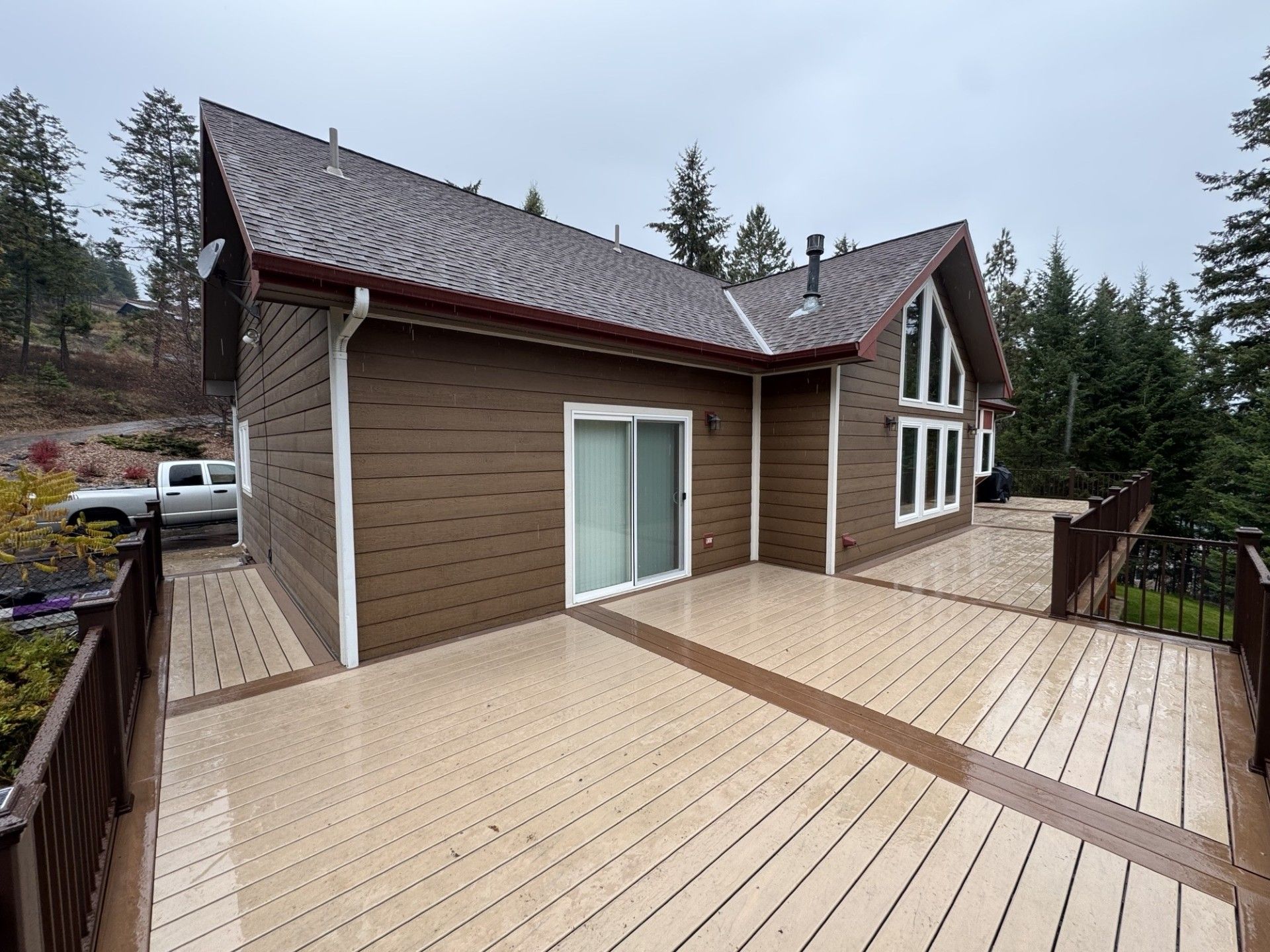Modern house with a large wooden deck and steep shingle roof in a wooded setting