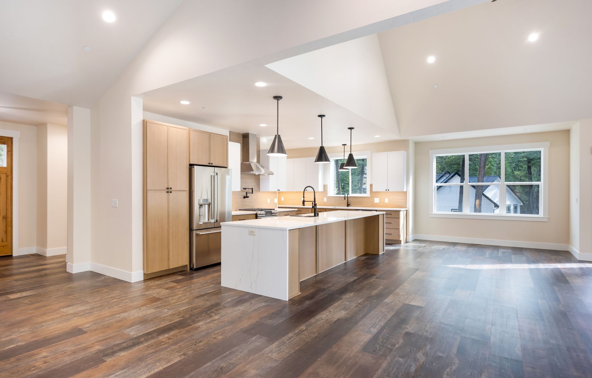 Bright open kitchen and living area with island, stainless appliances, wood floors, and large windows.